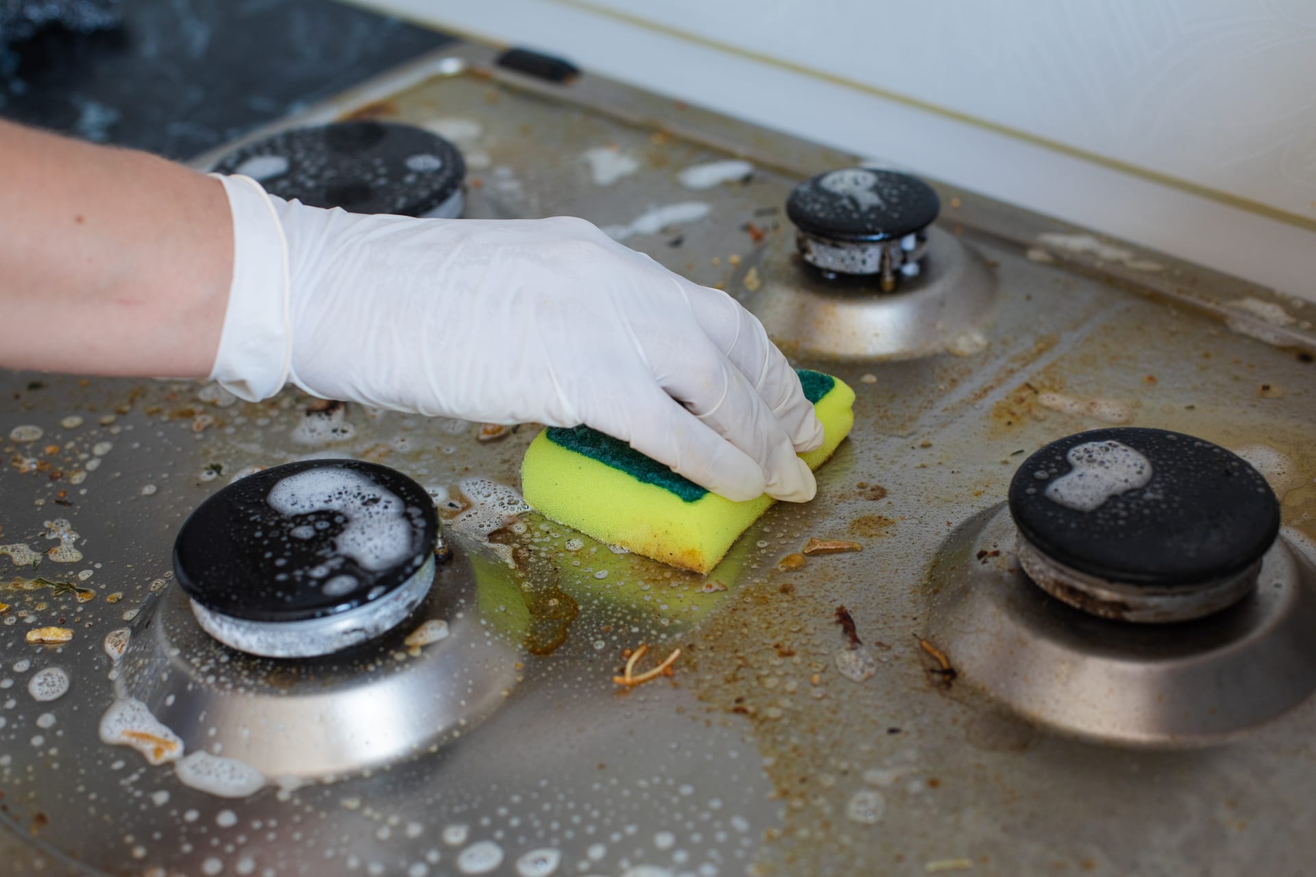 Gloved hand scrubbing a dirty stovetop with a sponge